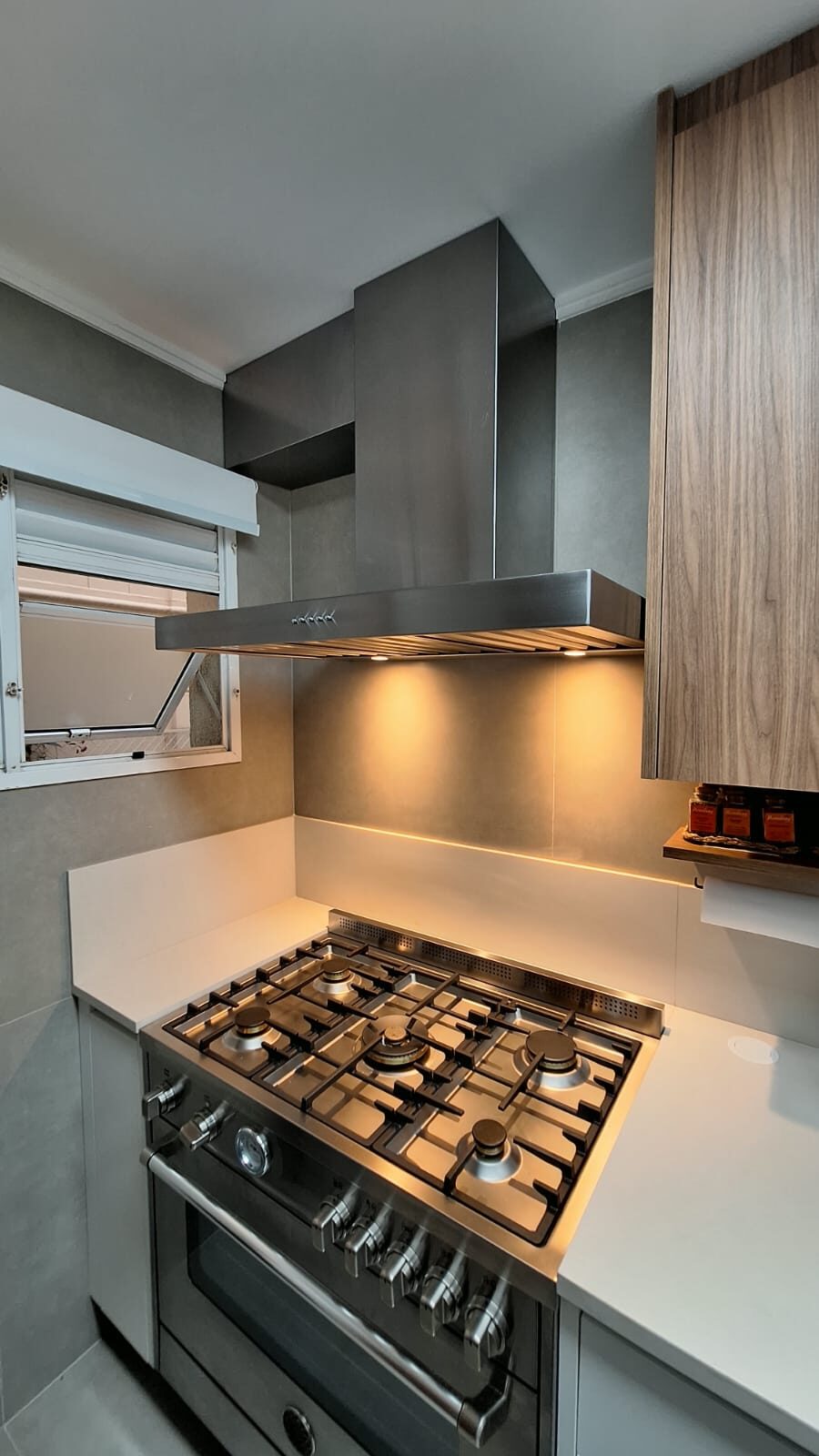 Coifa em aço inox com saída lateral pela janela instalada sobre fogão em cozinha