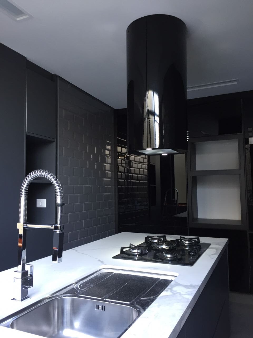 Coifa cilíndrica preta sob medida instalada sobre cooktop em ilha em cozinha integrada