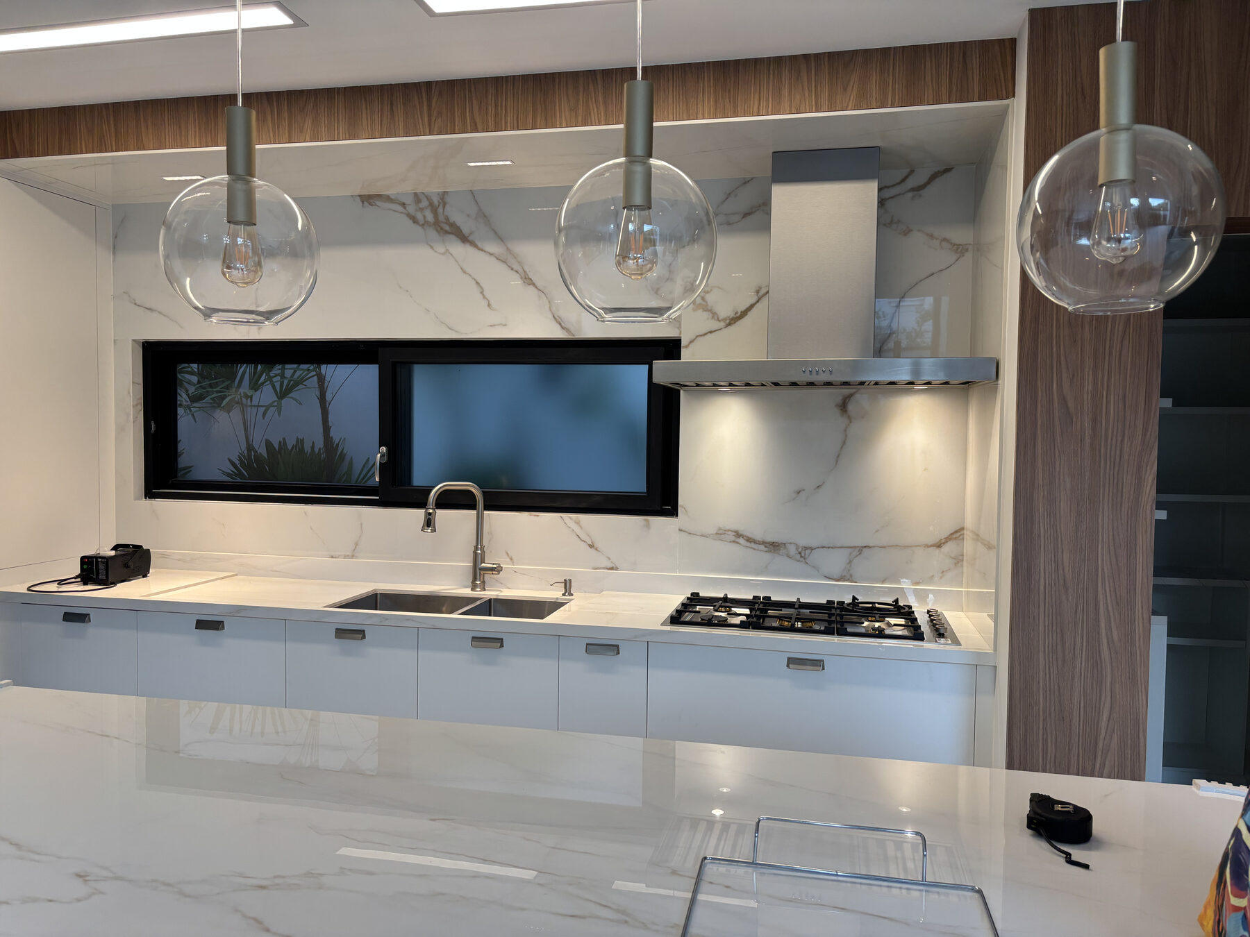 Coifa Slim de ilha em aço inox instalada sobre cooktop em cozinha contemporânea